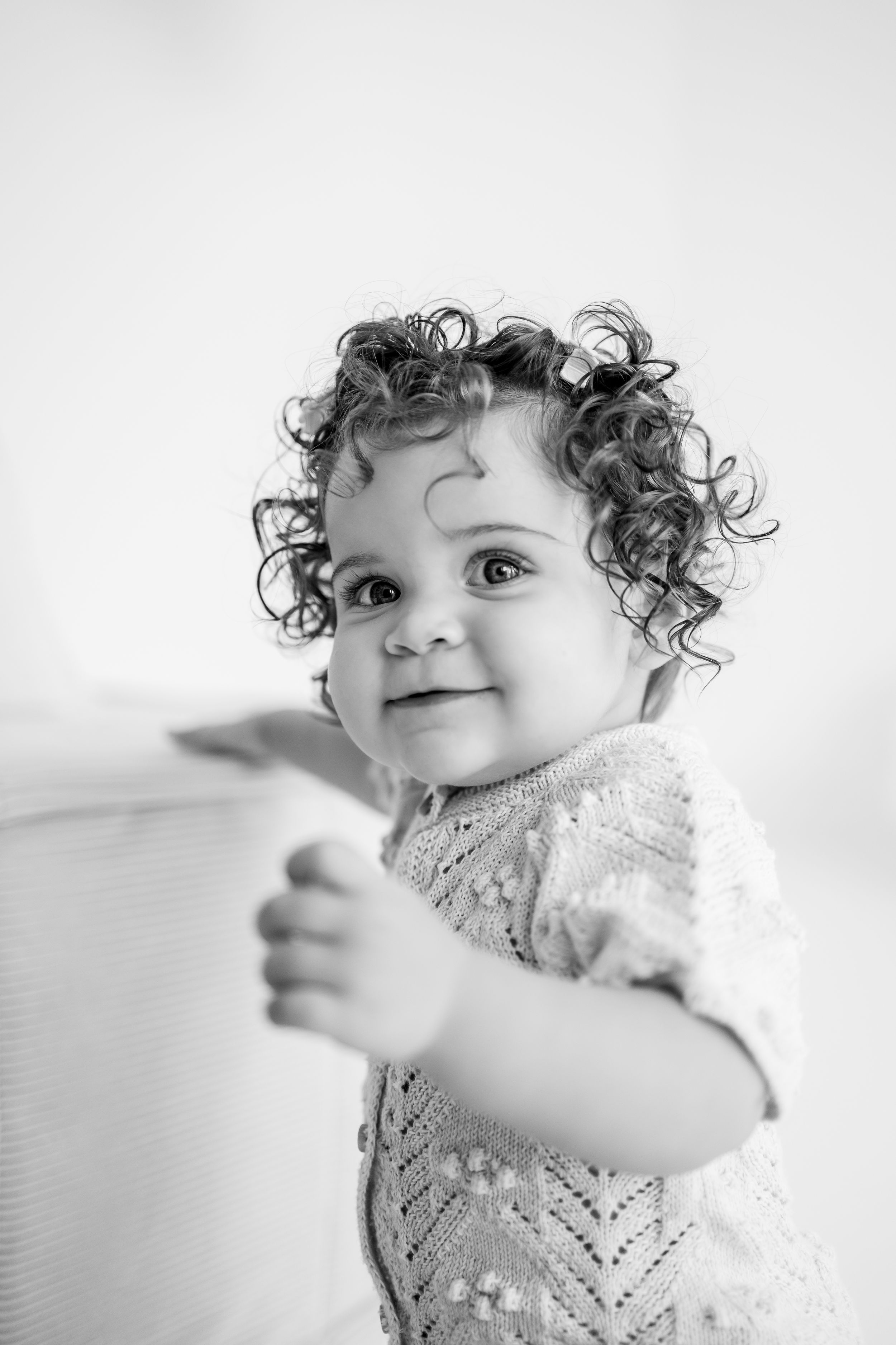 A sequence of black and white photos showing a small child with curly hair wearing lace, smiling and moving playfully.