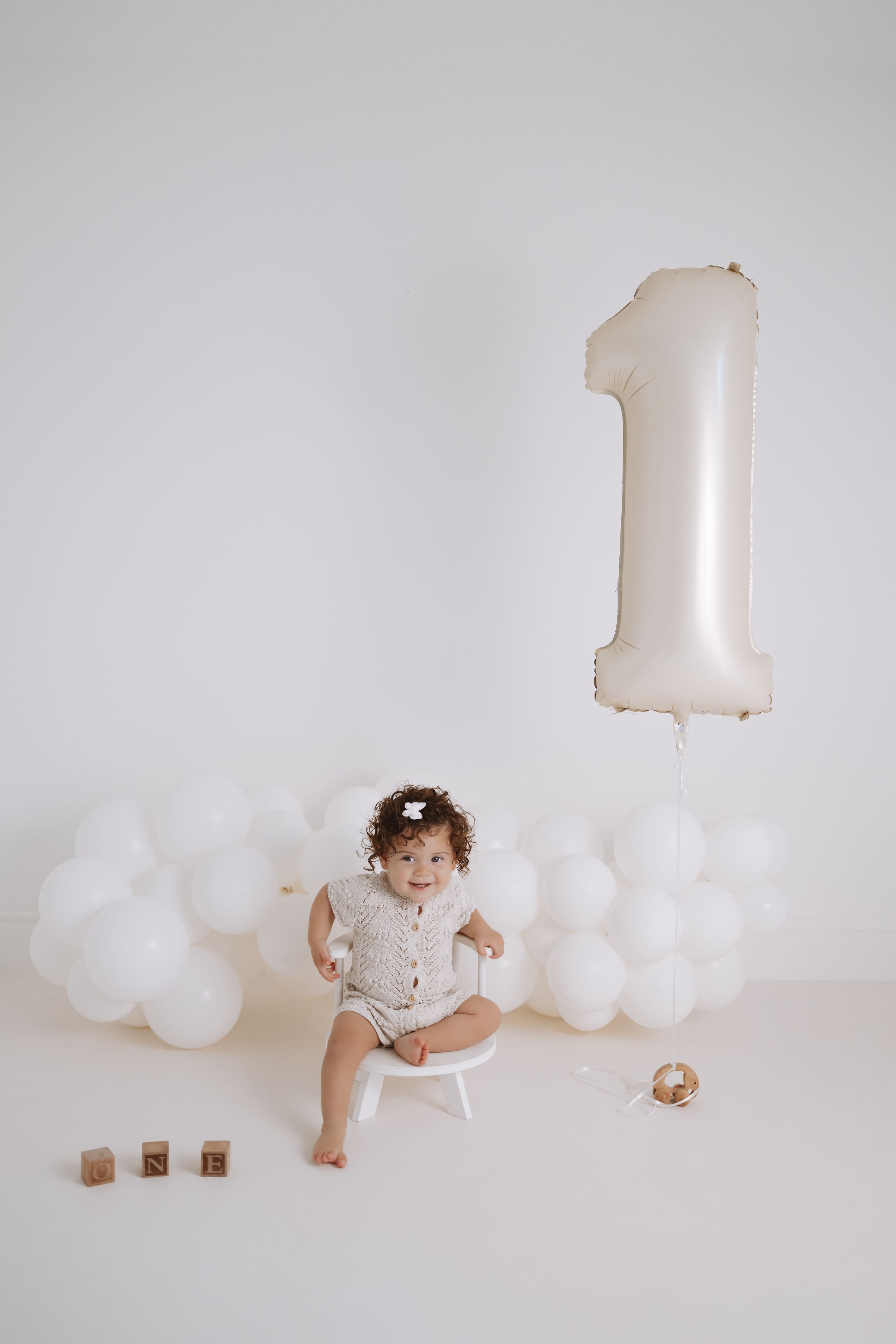 White minimalist first birthday setup with large number one balloon and white cloud balloons against light background.