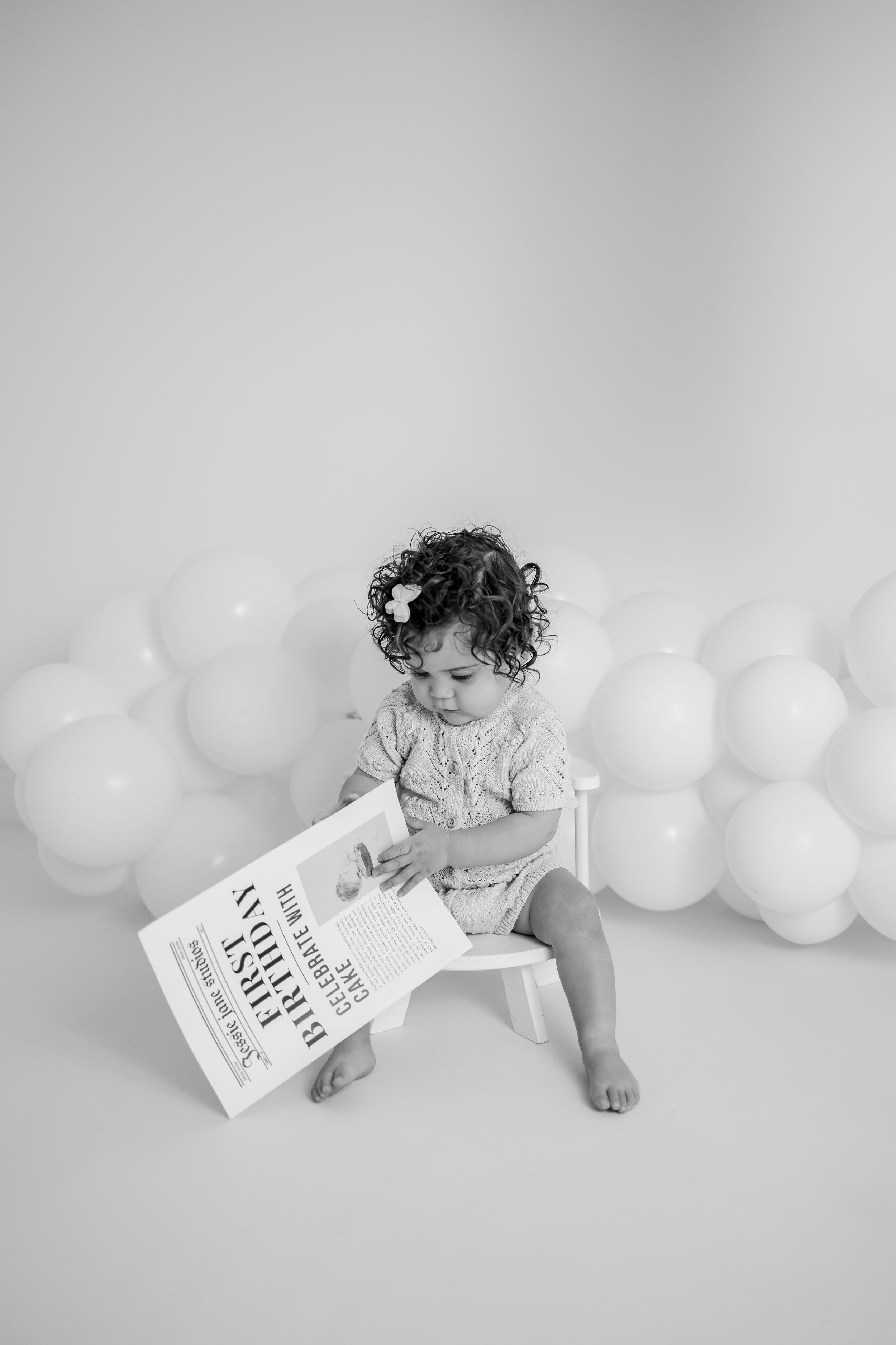 Black and white photo series showing a baby in white outfit with white balloons and a book in minimalist style.
