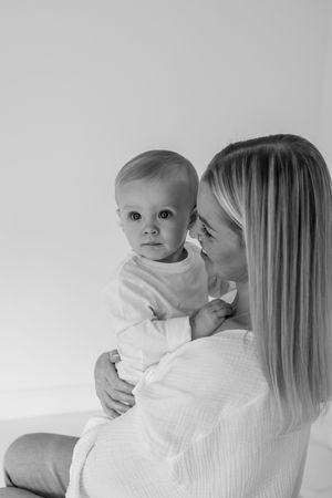A tender moment captured in black and white as a mother in white sweater holds and kisses her baby.