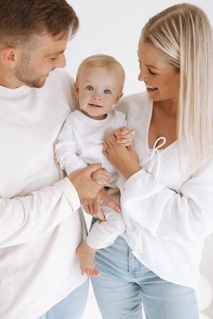A happy family wearing white tops share a tender moment together against a bright background.