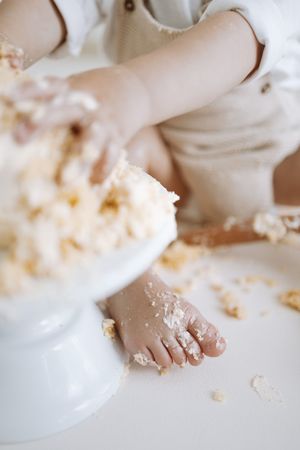 Close-up of tiny feet and cake crumbs during a cake smash photography session on white background.
