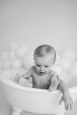 Black and white photo series of a baby playing and splashing in a white bathtub.