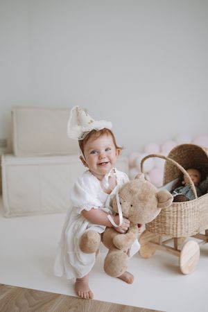 A child in white clothing plays with a teddy bear on a light-colored couch.