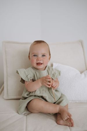 Baby in mint green outfit lies on white bedding showing various playful expressions and poses.