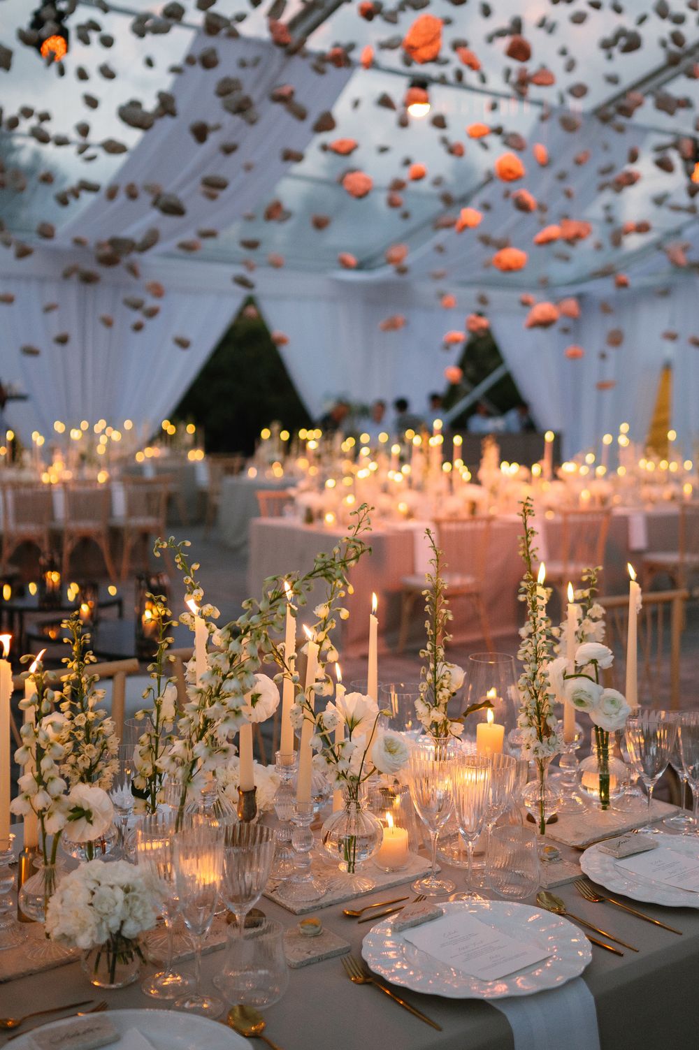 Romantic wedding reception table with floating candles and floral centerpieces under string lights.