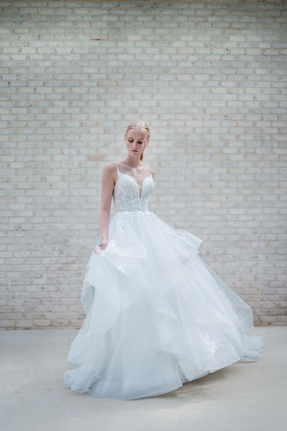 Ethereal bridal portraits showing a flowing white wedding gown against a brick wall backdrop.