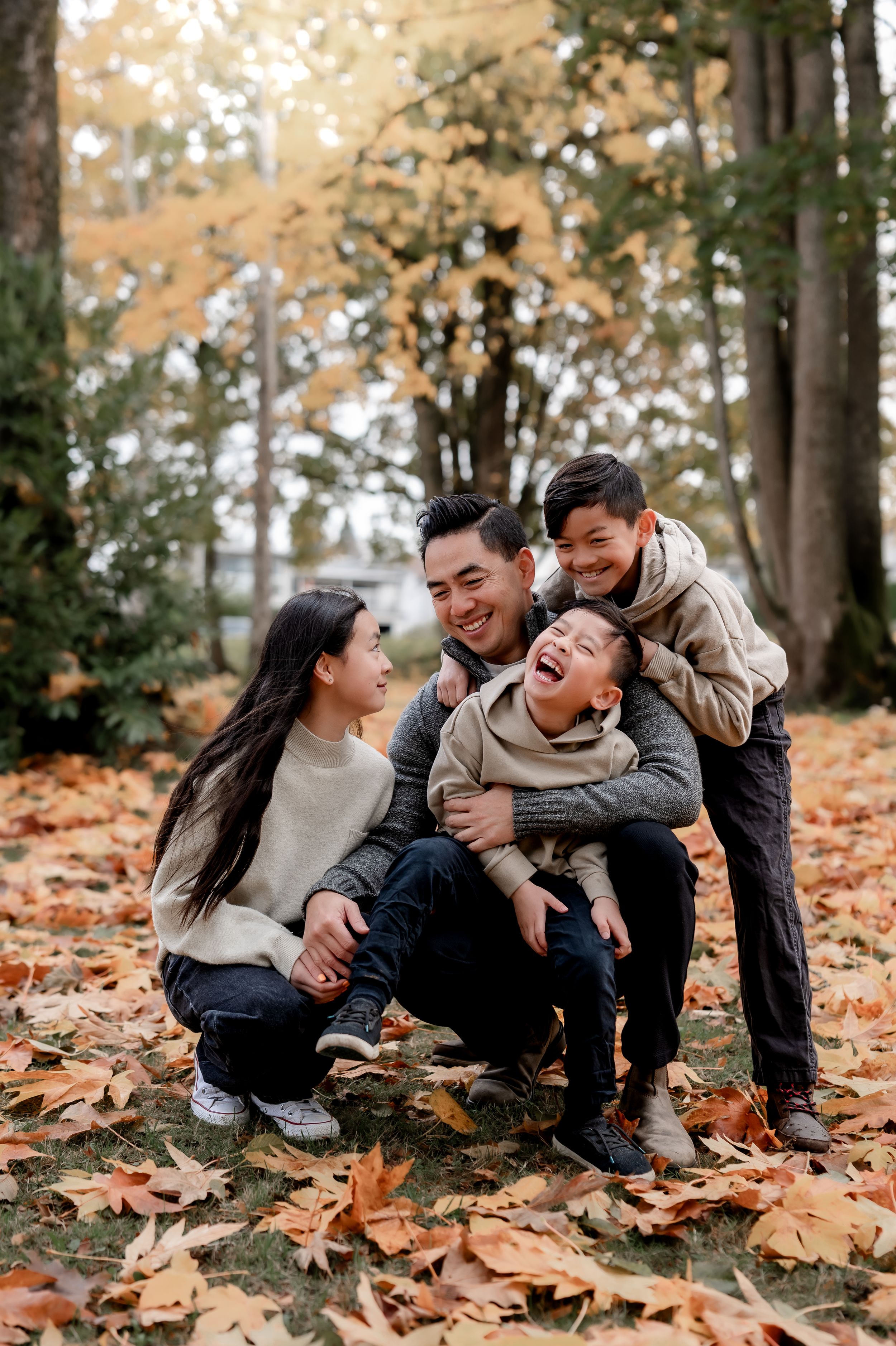 Family laughing together while sitting on autumn leaves in a forest setting.