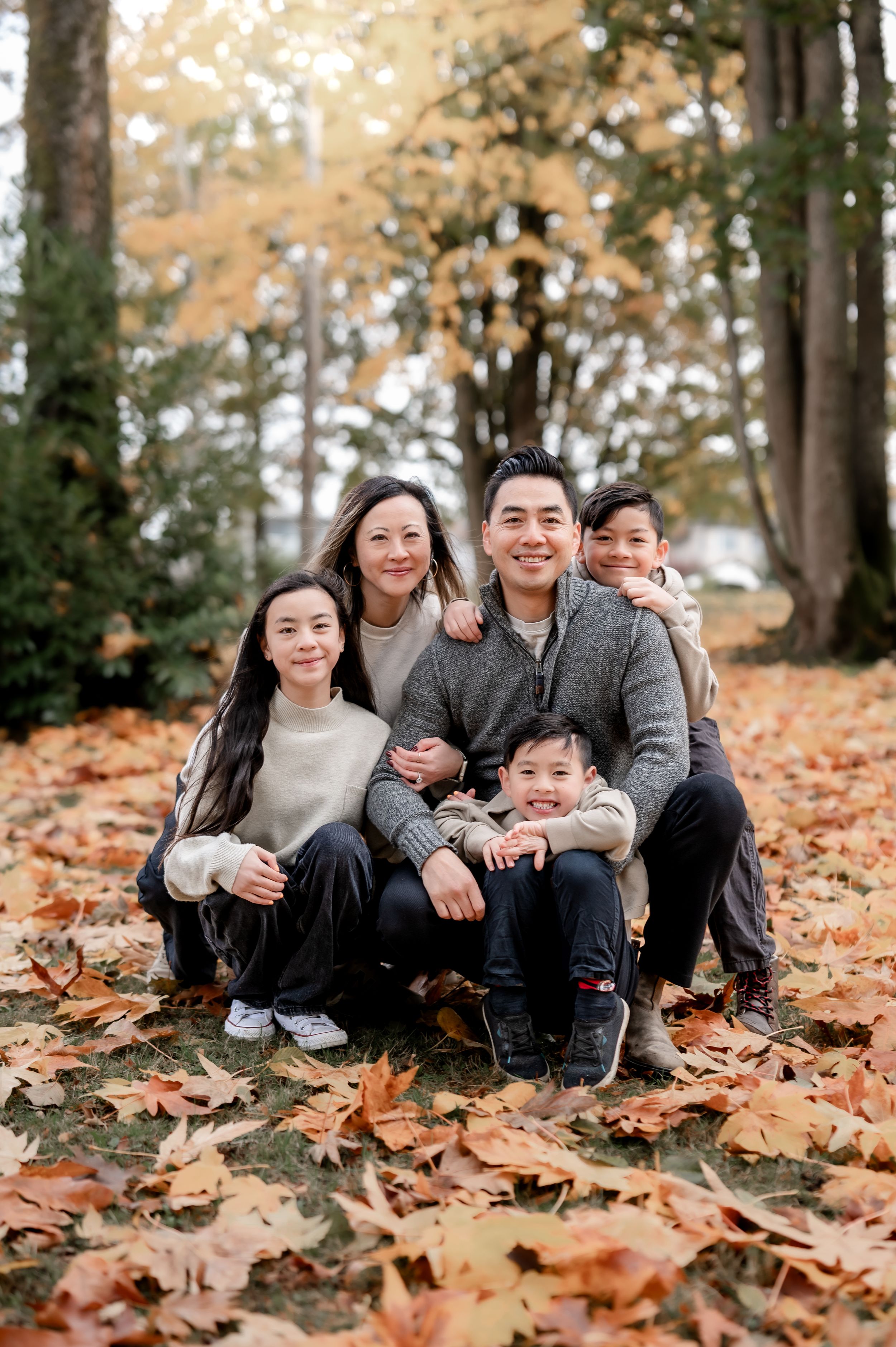 Family sitting together on fallen autumn leaves in a wooded area during a fall photo session.
