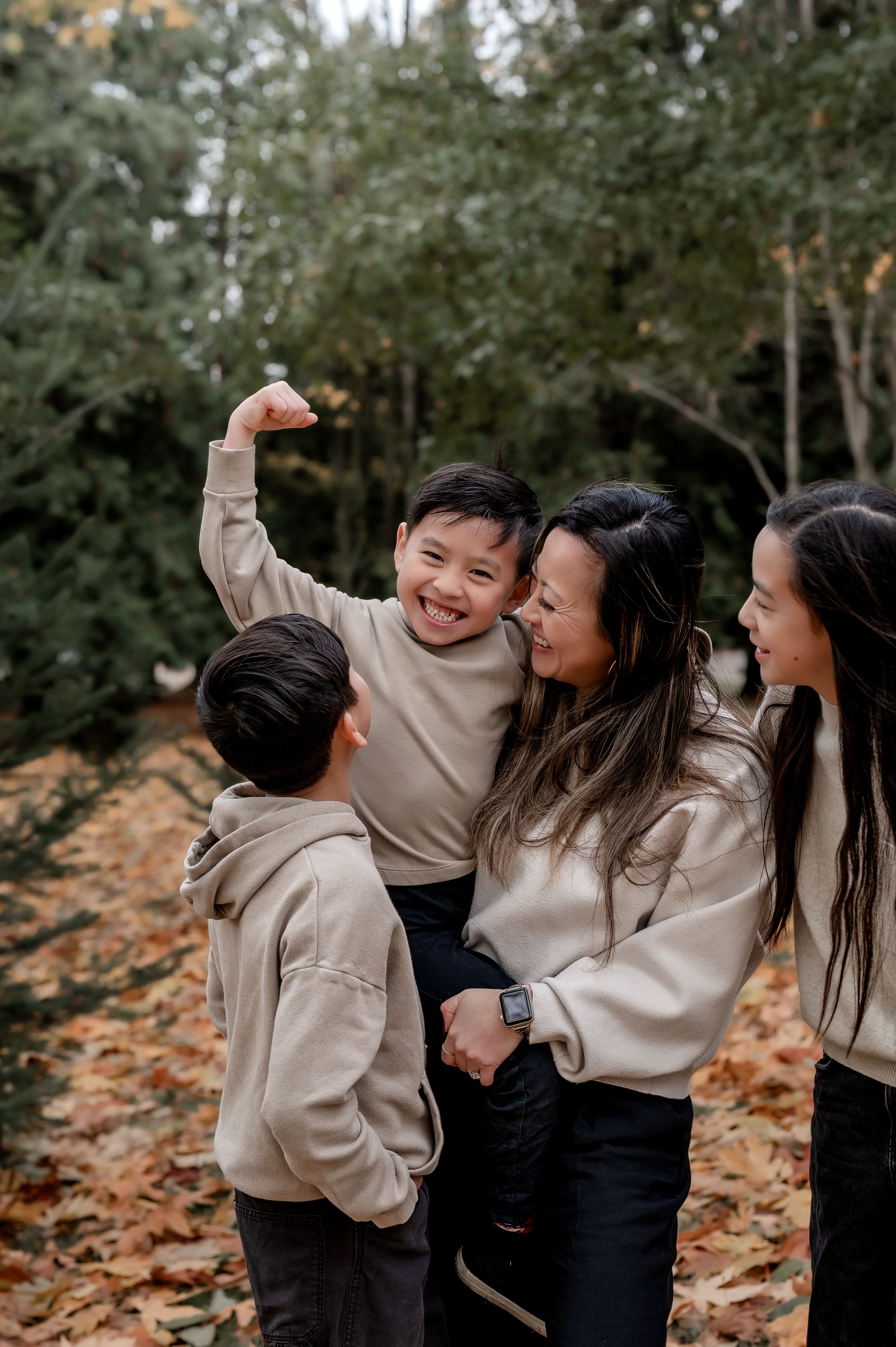 A joyful family wearing matching beige sweaters shares a candid moment together among fallen autumn leaves.