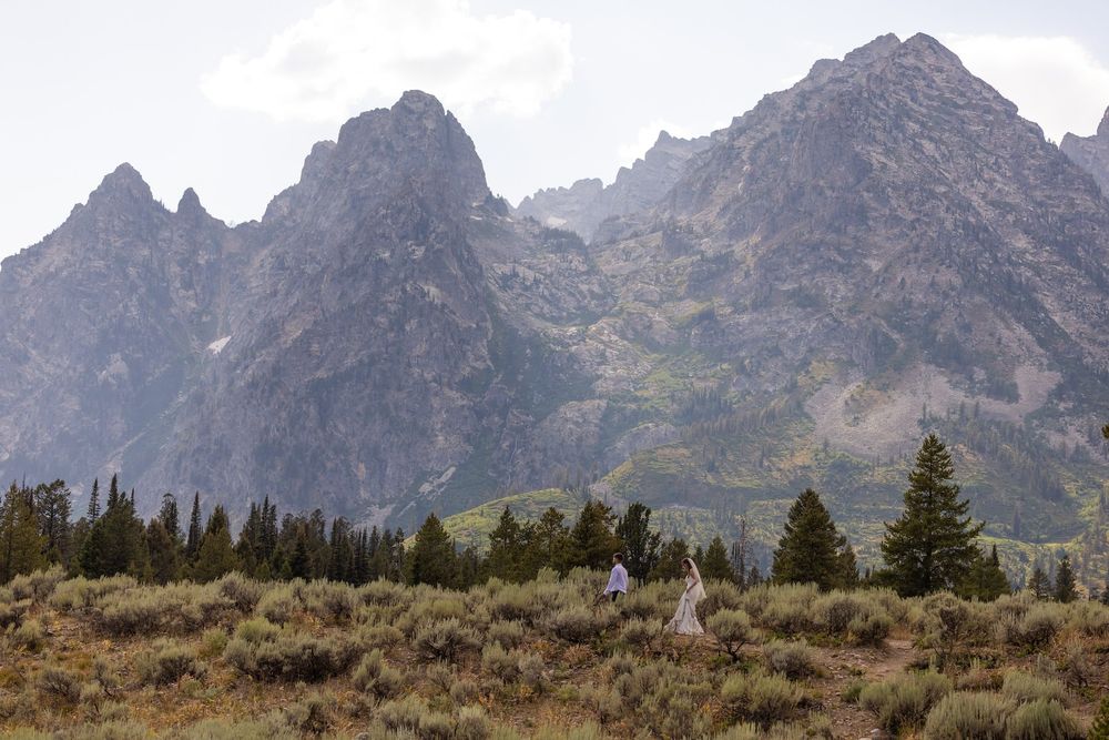 Rugged mountain peaks rise above evergreen trees in Grand Teton National Park on a cloudy day.