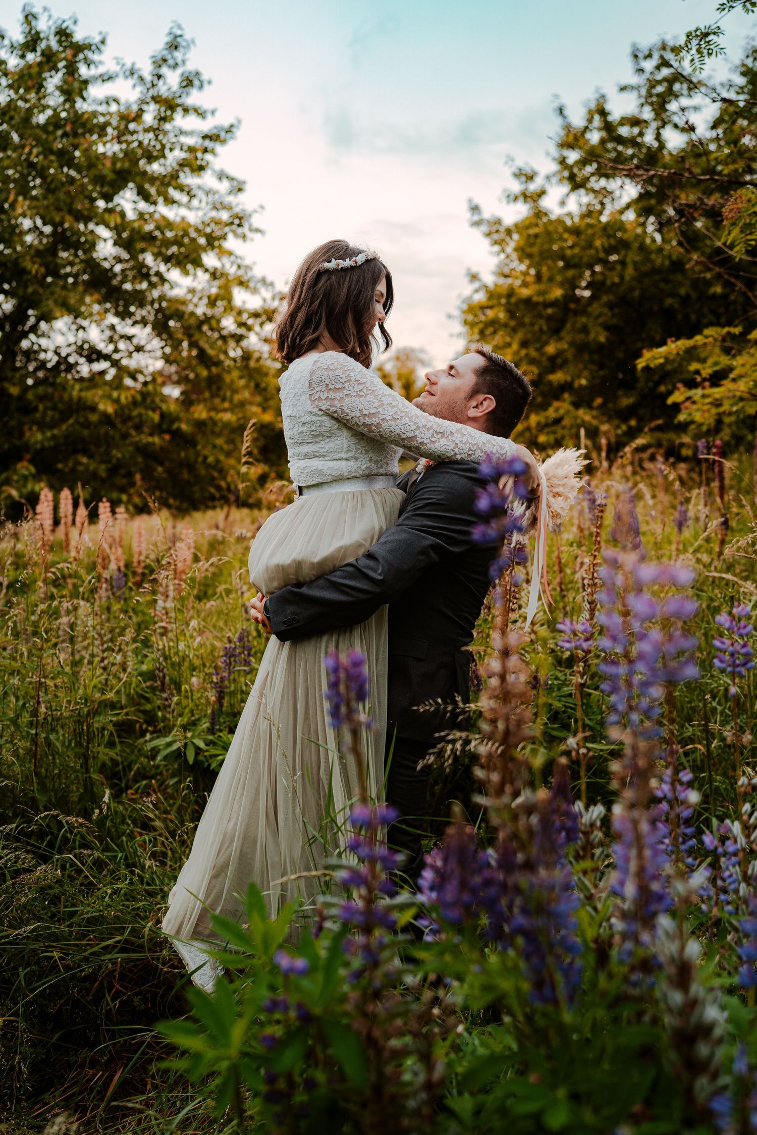 A romantic couple in white clothing shares an intimate moment in a wooded setting during golden hour.