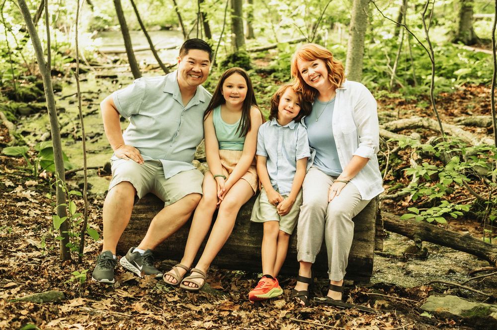 Happy family of four smiling together on a wooden bench surrounded by lush green forest trees.