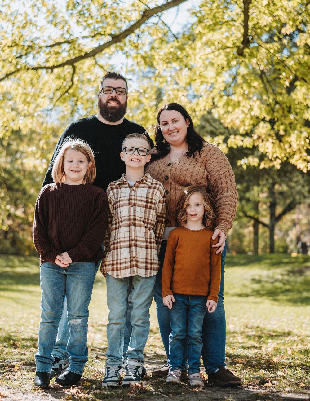 Family of five posing together on autumn day with golden trees in background.