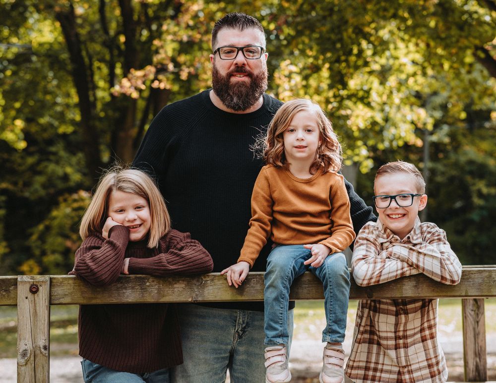 Family sitting together on a wooden fence during a fall photo session.