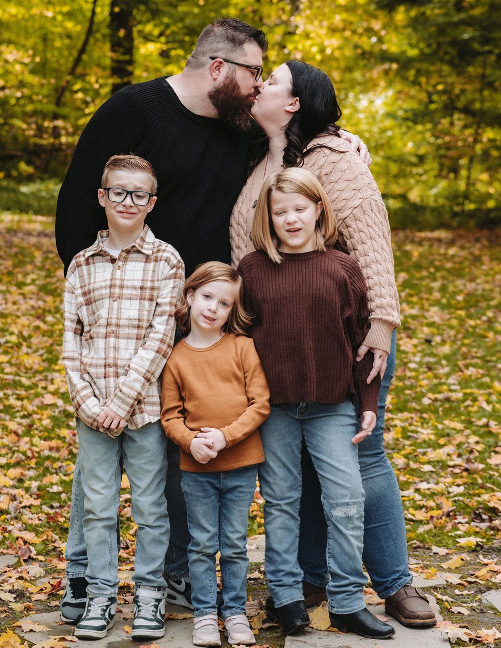 Family members standing together on fallen autumn leaves in coordinated casual wear.