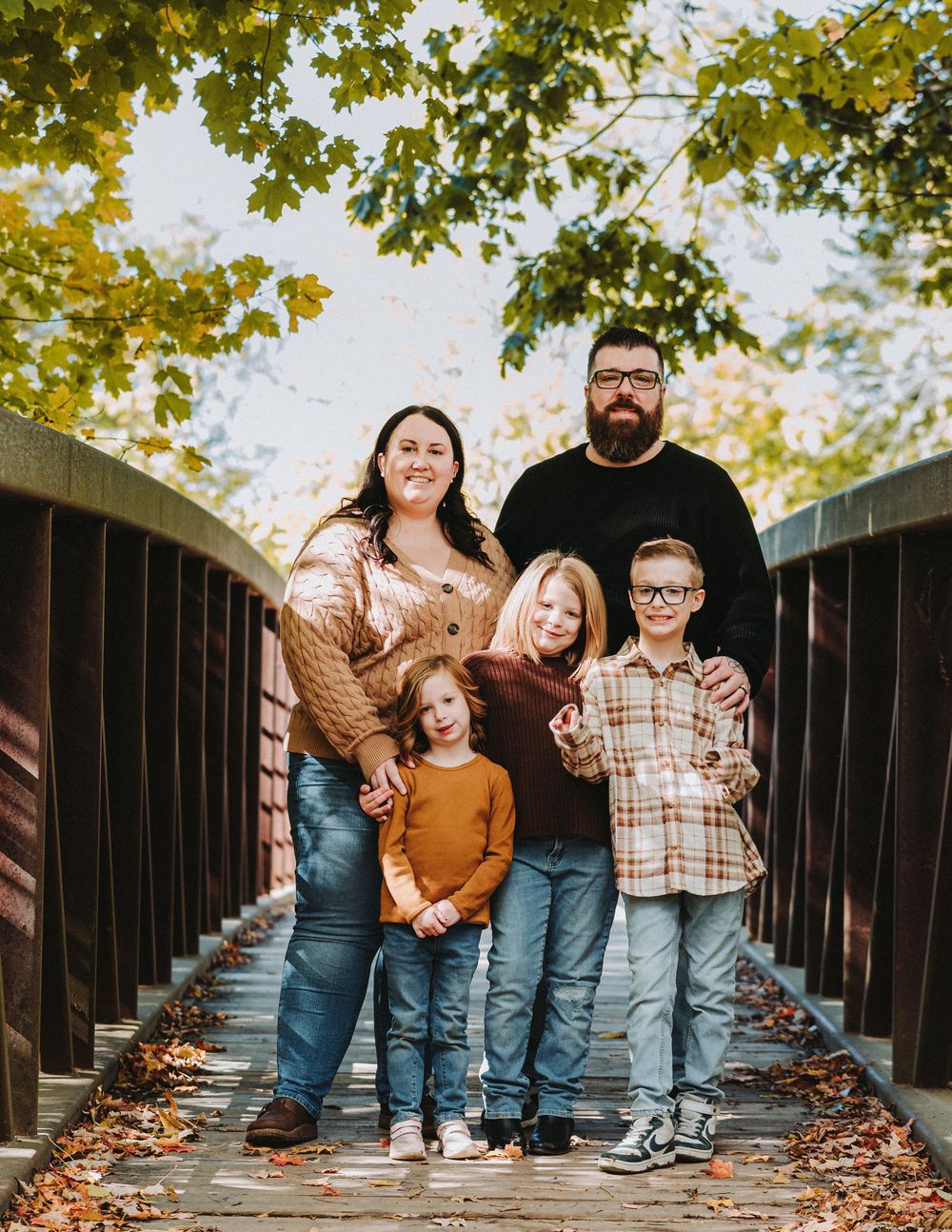 Family posing together on a wooden bridge covered in fallen autumn leaves.