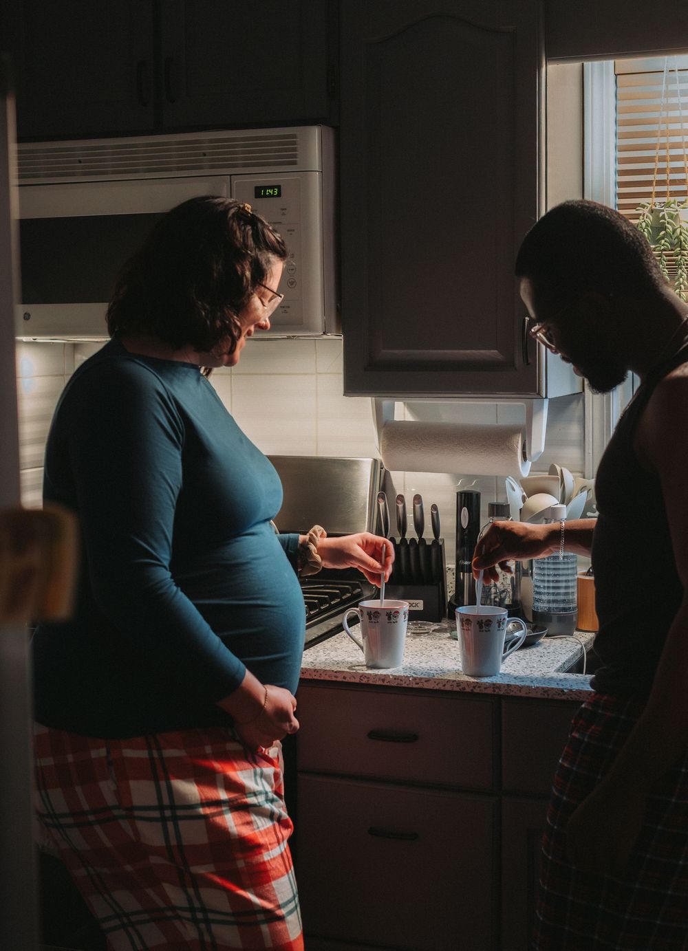 Person in plaid pajamas standing in a dimly lit kitchen.