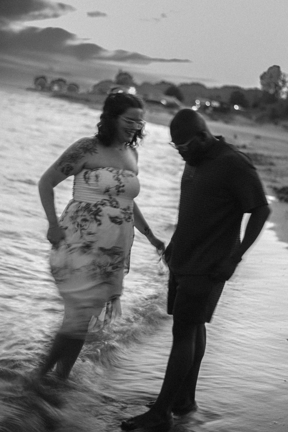 Black and white silhouettes of a couple walking along the shoreline at dusk.
