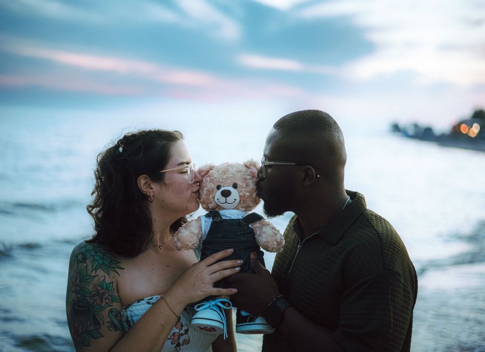 A couple shares intimate moments on the beach with a teddy bear and ultrasound photo.