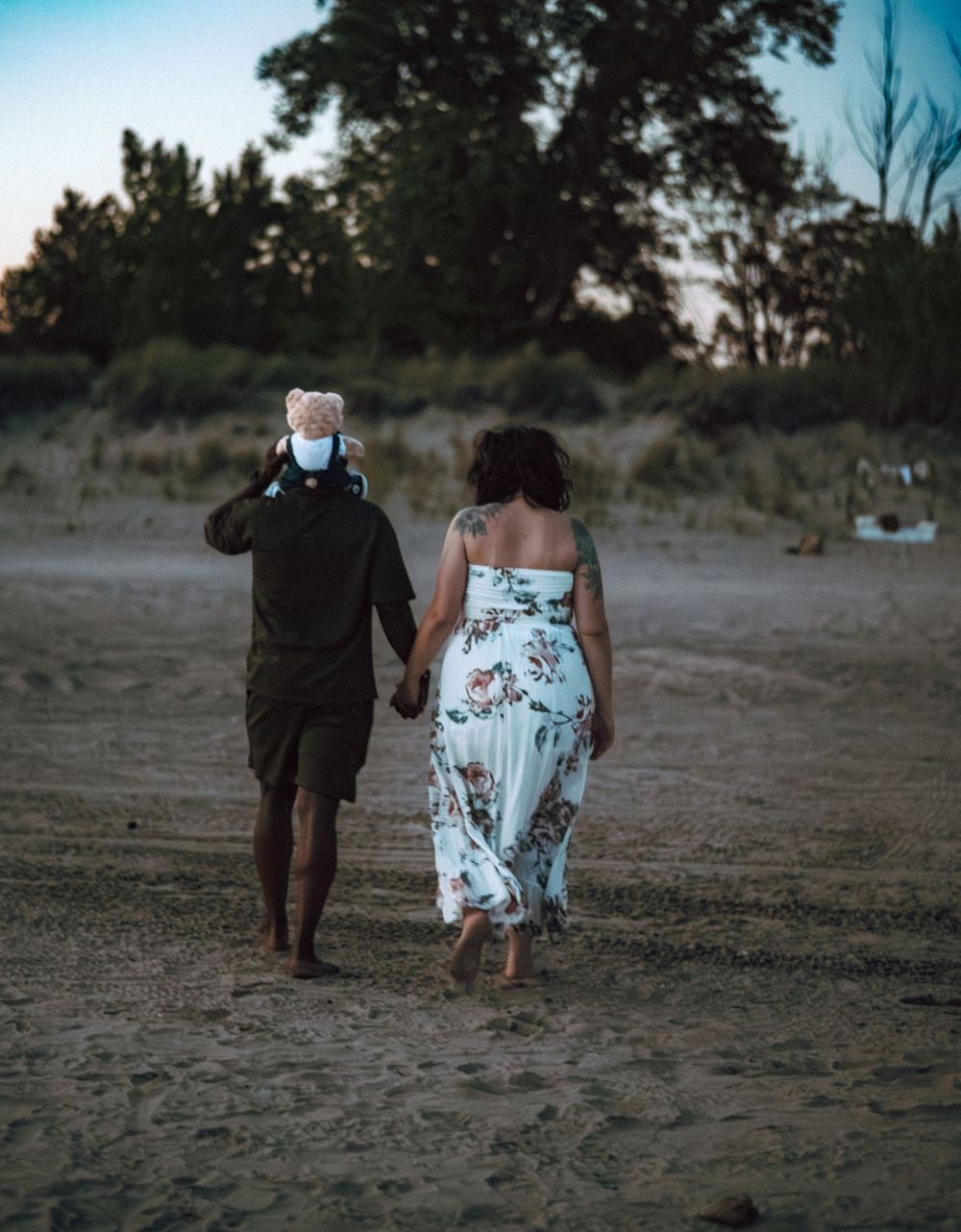 A couple walks hand in hand across a sandy beach during golden hour.