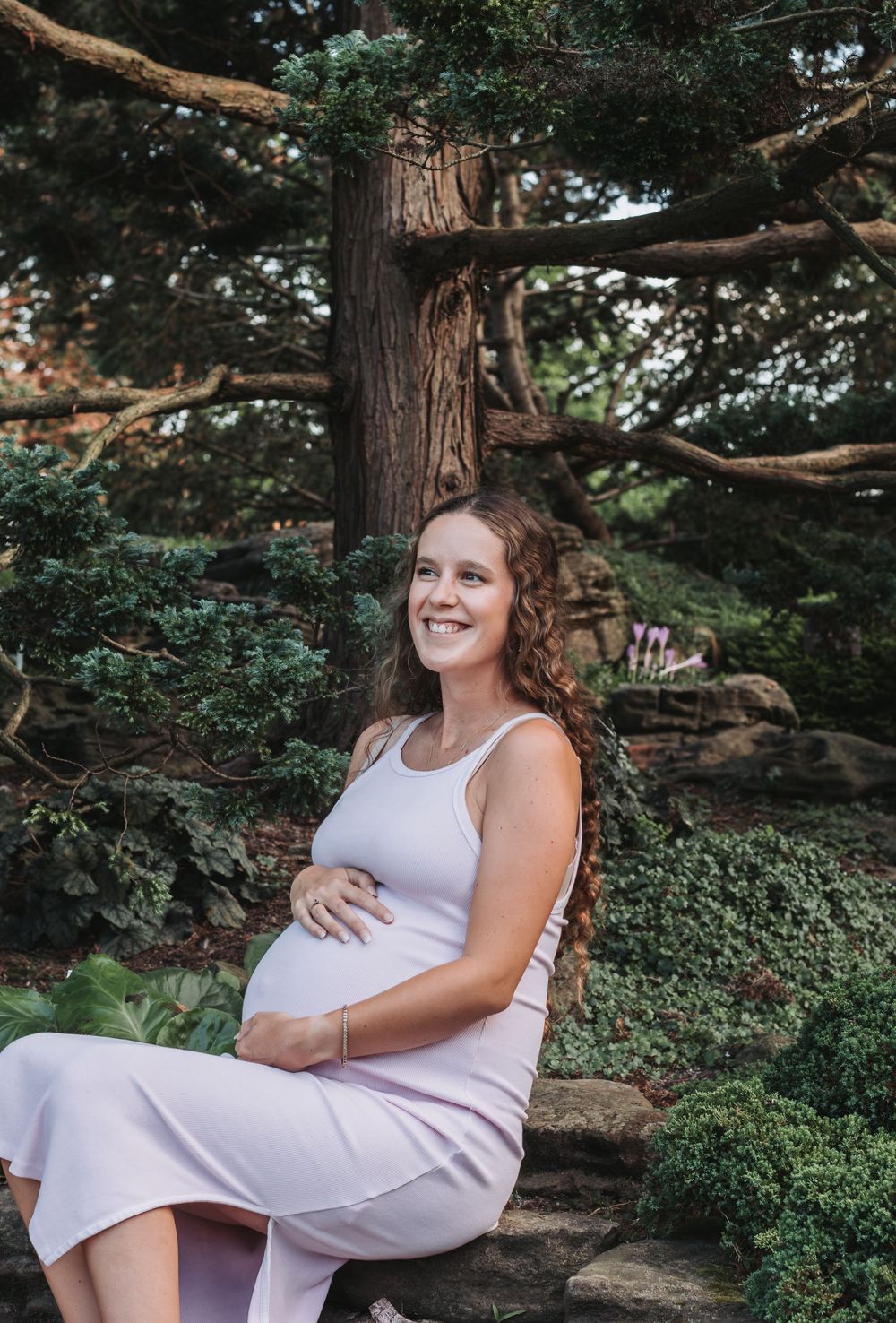 Maternity portrait in white dress against natural woodland backdrop.