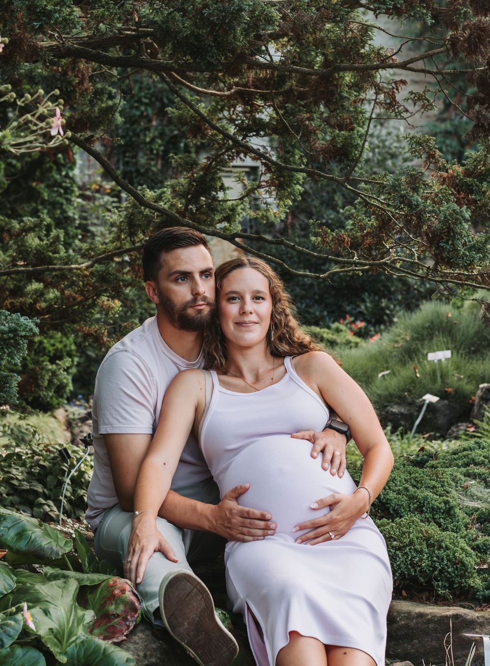 Maternity photo of couple embracing in a lush garden setting with greenery in the background.