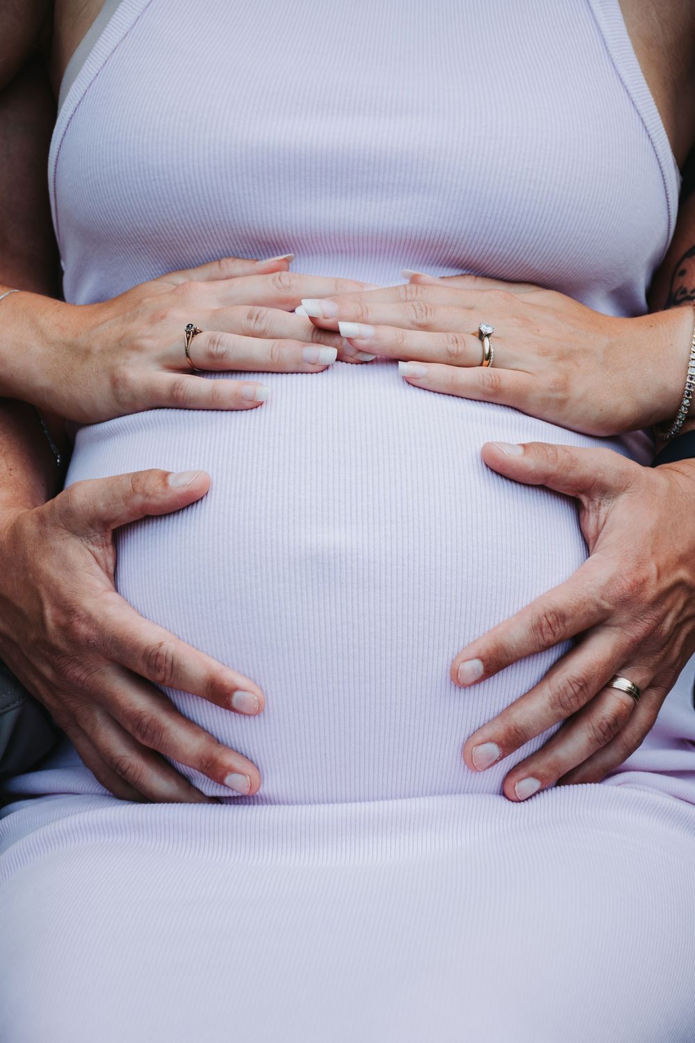 Close-up of hands forming a heart shape on a pregnant belly in a white dress.