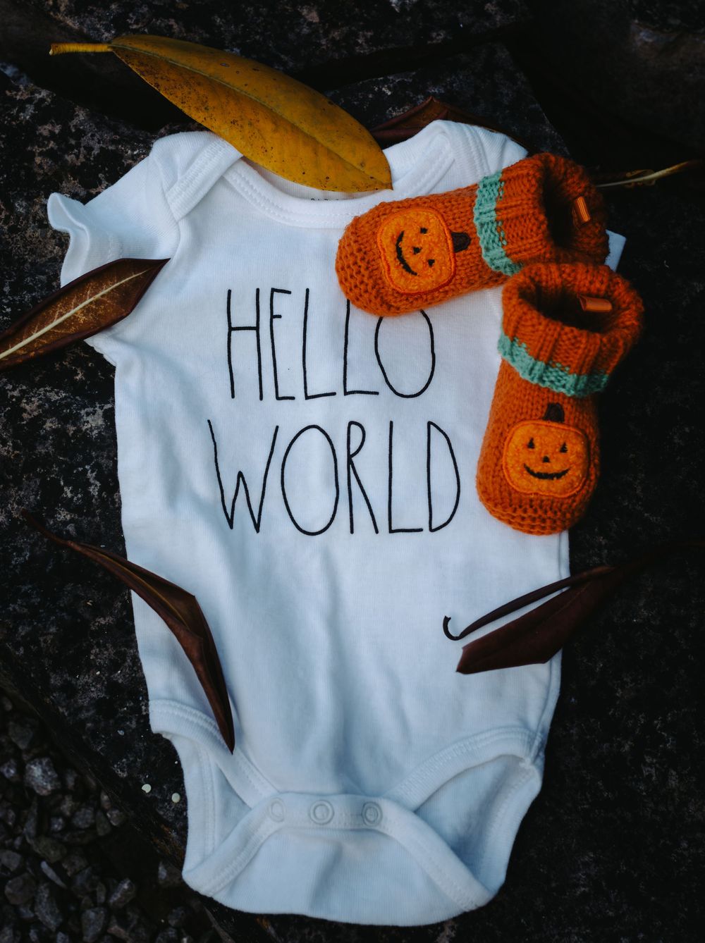 White baby onesie with 'Hello World' text and orange pumpkin-themed booties.
