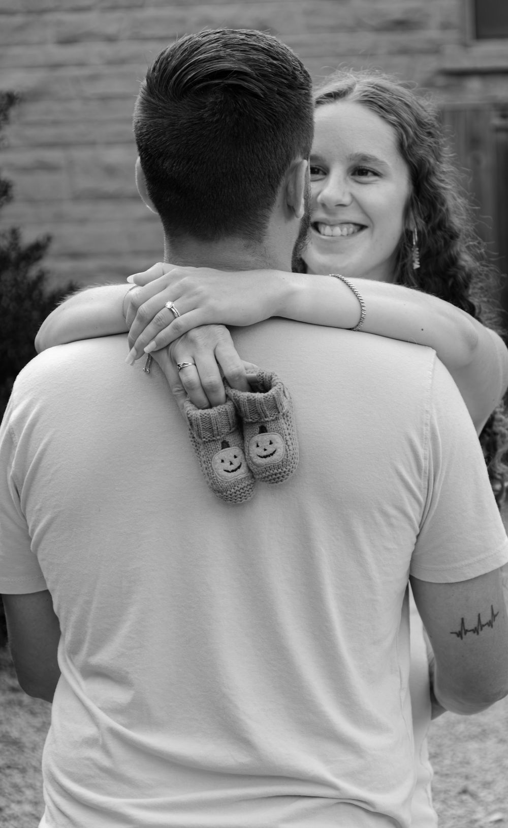 Black and white pregnancy announcement photo with couple holding baby booties.