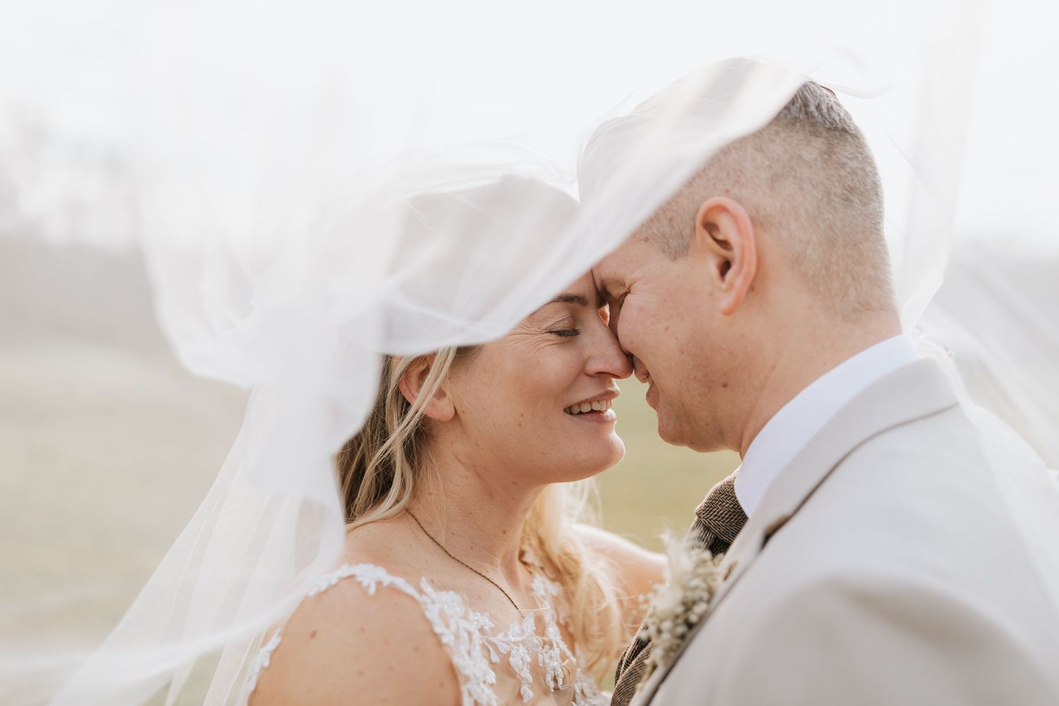 A bride in a flowing white wedding gown and veil walks along a gravel path on her wedding day.