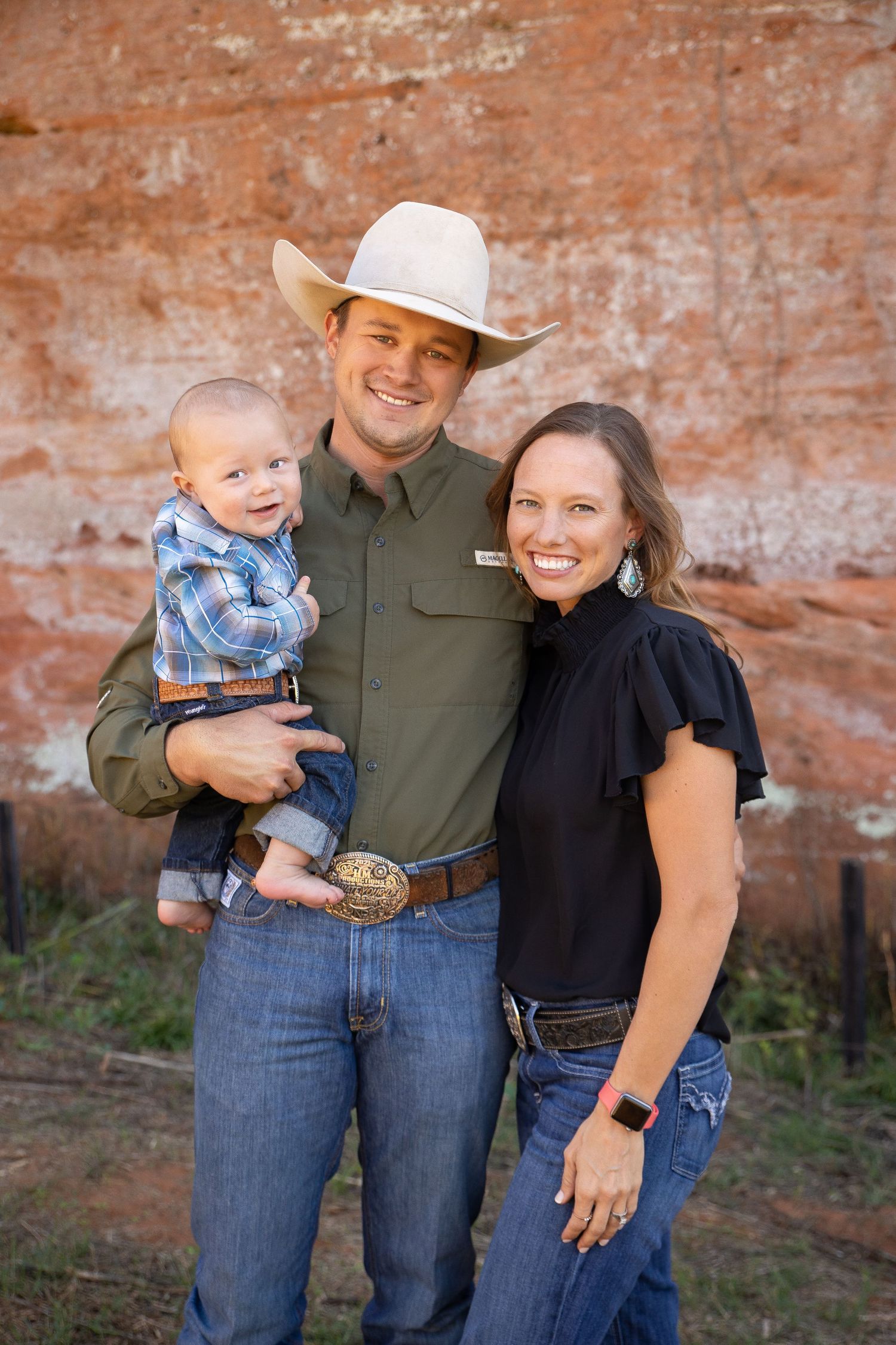A family poses together against a rustic red brick wall outdoors in casual western attire.