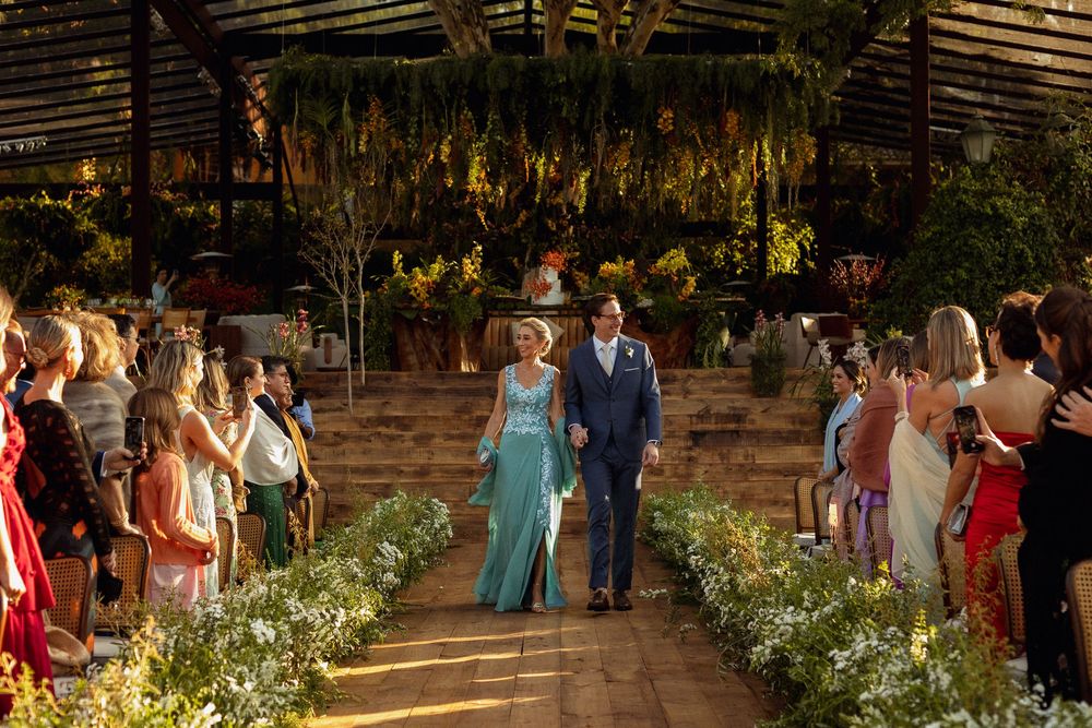 Wedding guests mingle on a rustic wooden deck decorated with floral arrangements and string lights.