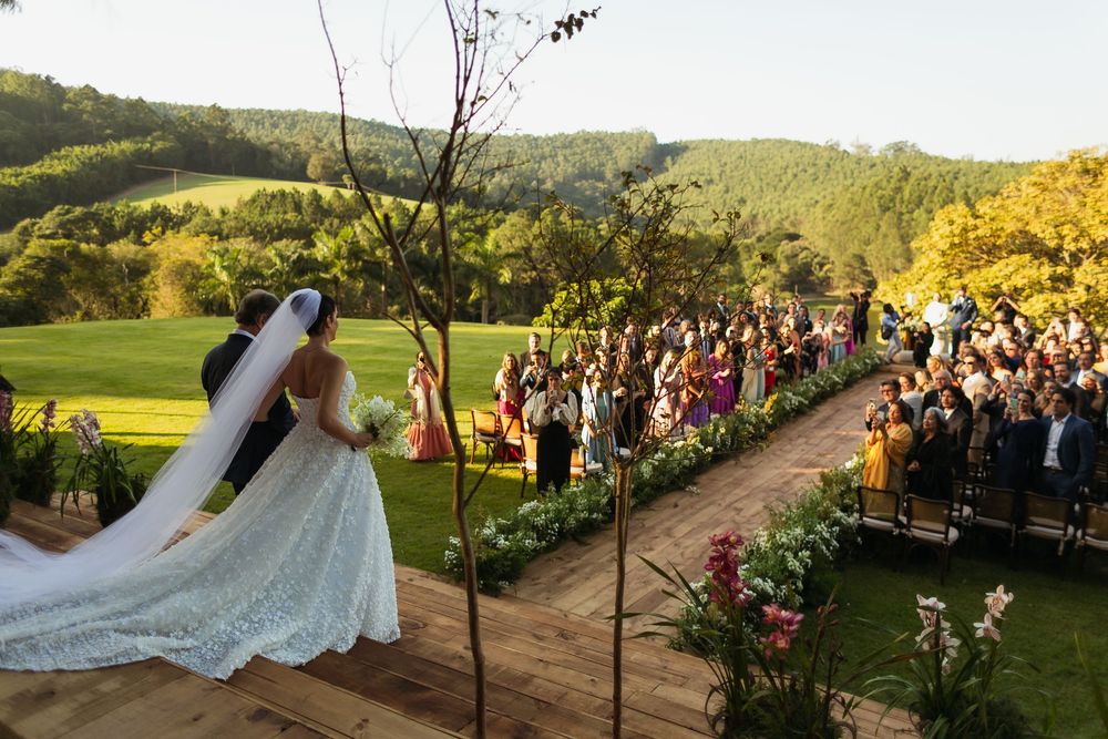 A scenic outdoor wedding ceremony with rolling hills and a large crowd of guests.