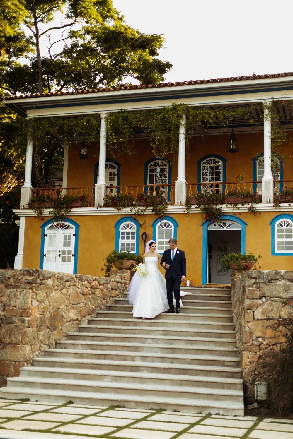 Yellow colonial-style building with white columns and blue windows serves as elegant wedding venue backdrop.