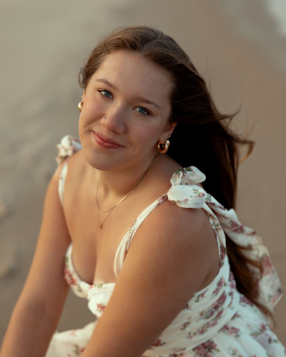 A portrait in warm lighting shows someone wearing a floral summer dress with tie straps against a soft blurred background.