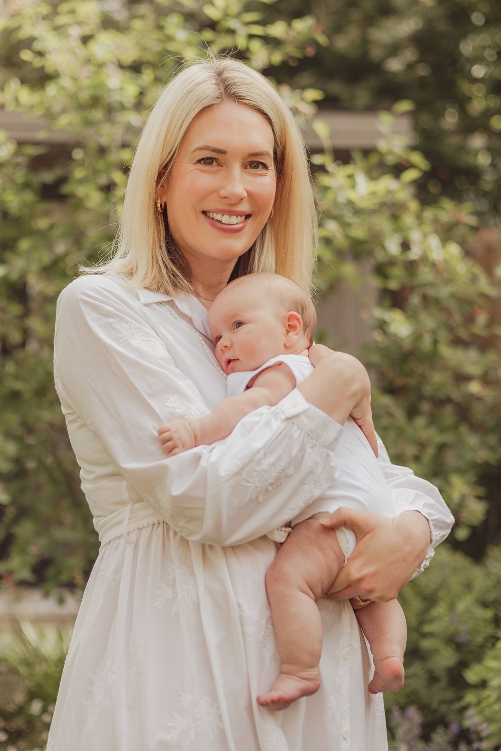 a photo of a mother holding her baby to her chest, and smiling whilst the baby rests her head on her chest