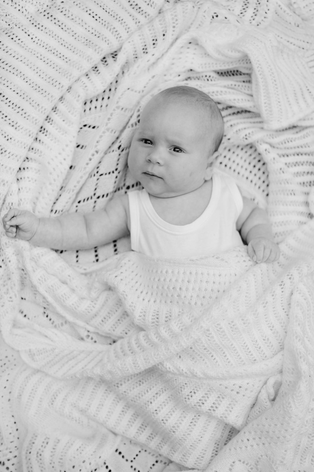 a black and white photo of a baby laying on the grass in a white vest, wrapped in a white blanket