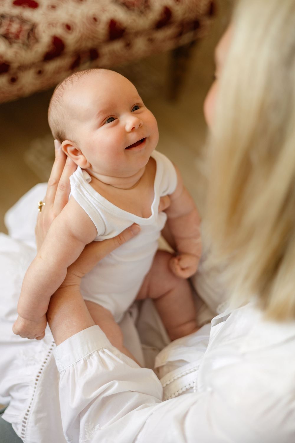 an image of a baby in a white vest, gazing up at its mother with a smile on its face