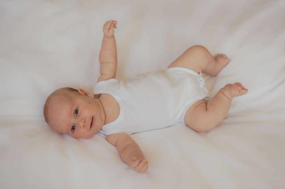 an image of a baby in a white vest laying on a white sheet