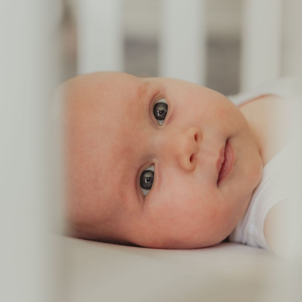 a baby photographed through the bars of its cot
