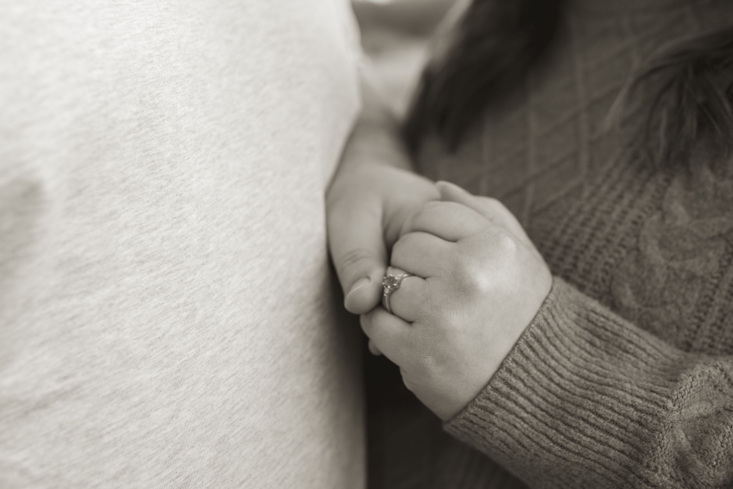 Close-up of hands with engagement ring against a soft white background.