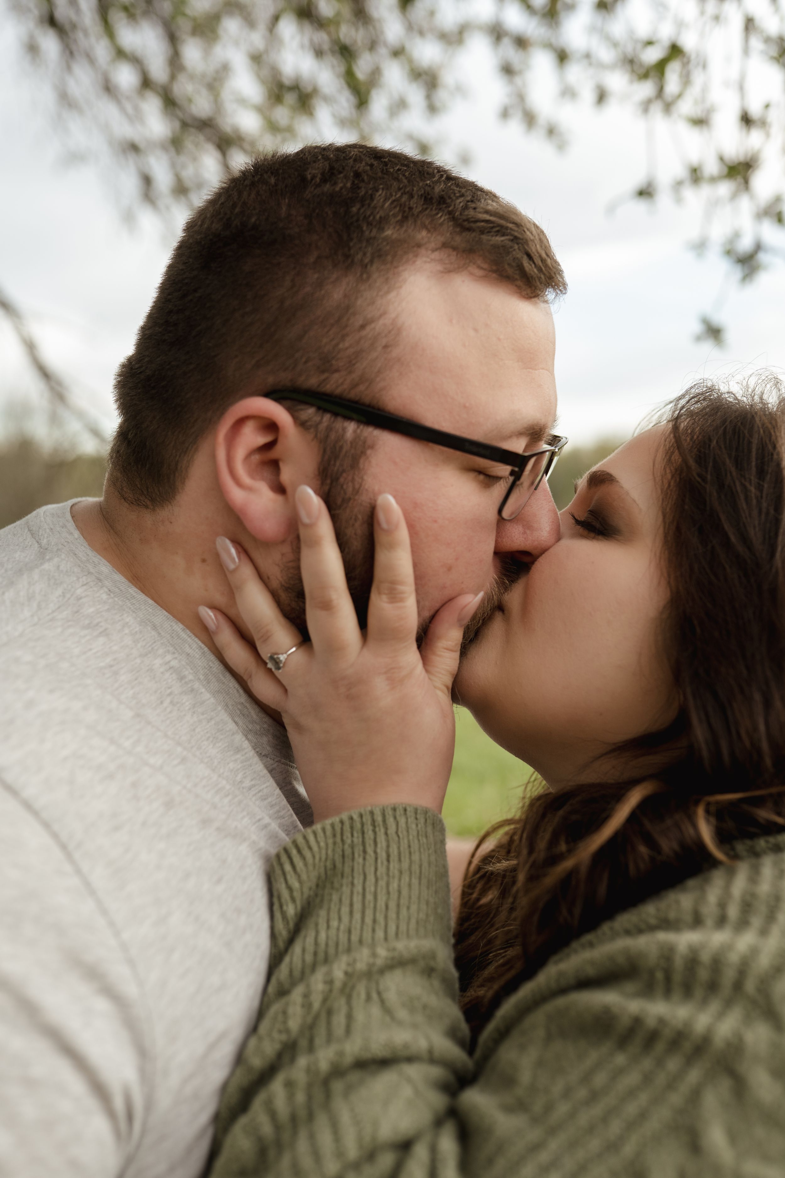 A romantic kiss captured in soft natural lighting under trees.