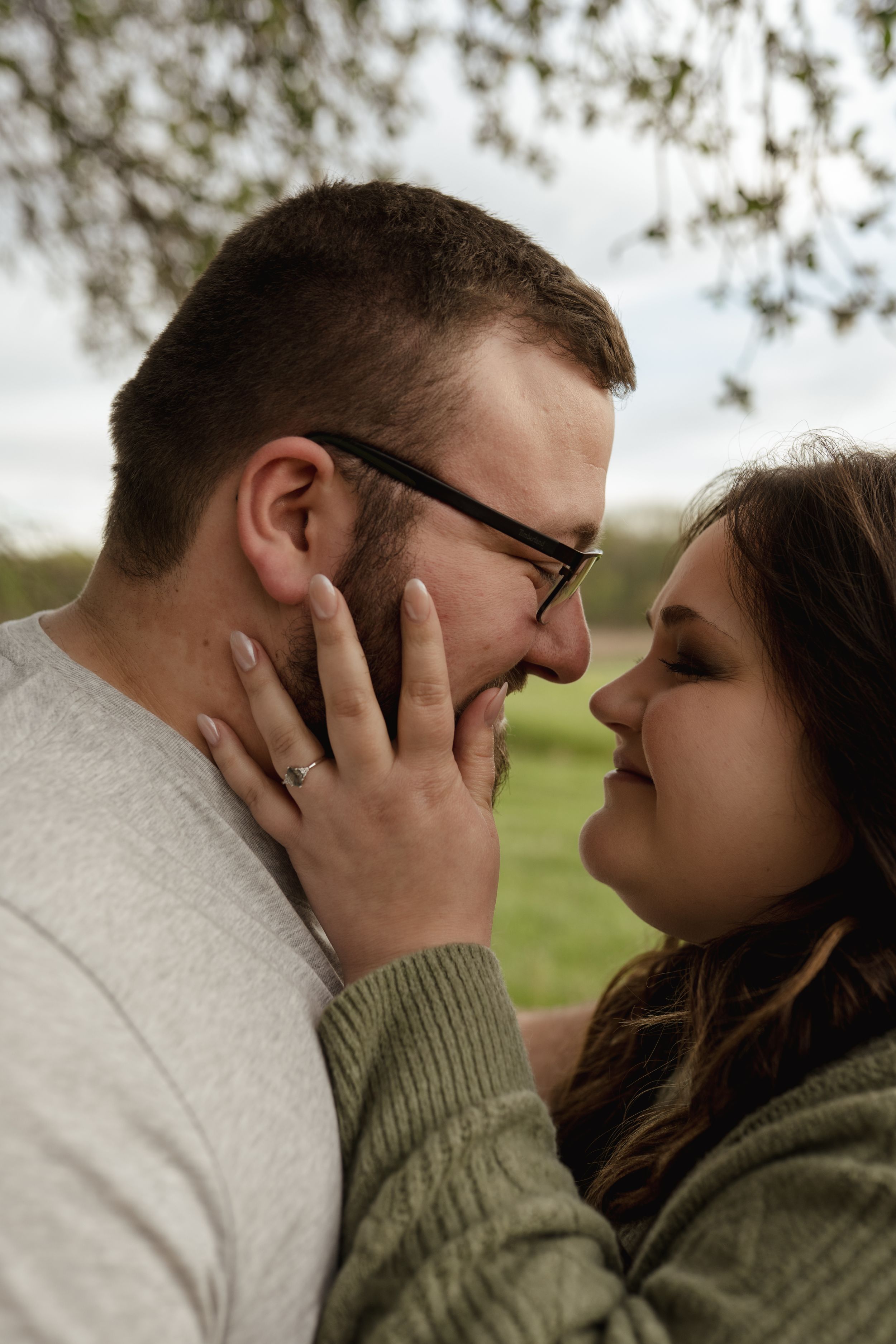 A romantic couple shares an intimate moment outdoors with soft lighting and natural scenery in the background.