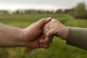 Close-up of hands reaching toward each other with an engagement ring visible.