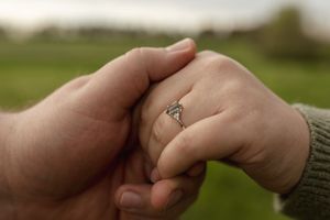 Detail shot of hands touching gently with an engagement ring prominently displayed.