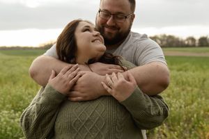 A couple embraces in a grassy field wearing casual clothing during an engagement photoshoot.