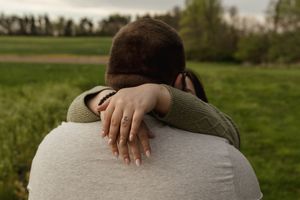 A romantic couple embraces in a green field during golden hour.