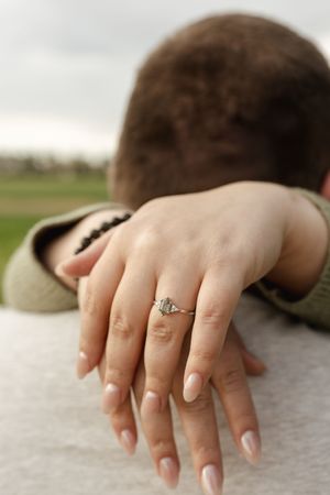 Close-up shot of a hand wearing an engagement ring against a gray sweater.