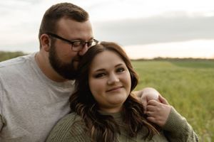 A couple shares a romantic moment in a grassy field at sunset.